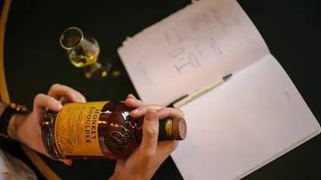 Person hält Whiskeyflasche mit offenem Notizbuch.
