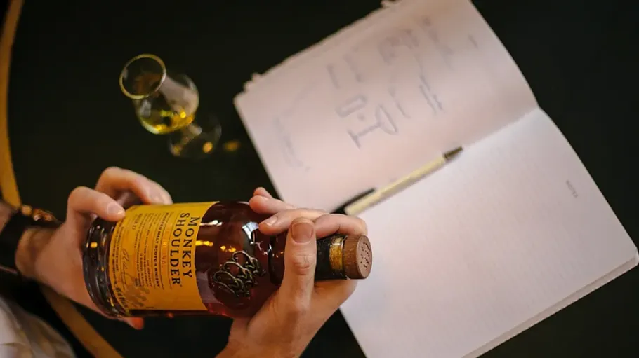 Person holding whiskey bottle with open notebook.