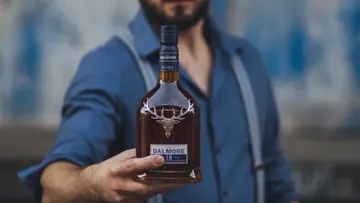 Person holding a Dalmore whiskey bottle outdoors.