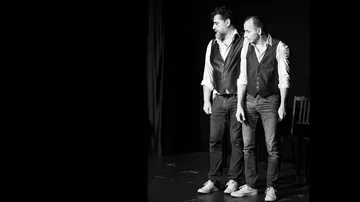 Two men in vests perform on stage.