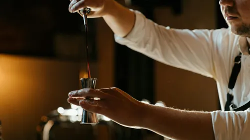 Barkeeper gießt Flüssigkeit in Jigger, schummrige Barbeleuchtung.