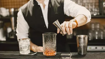 Bartender pours liquid into glass at bar.