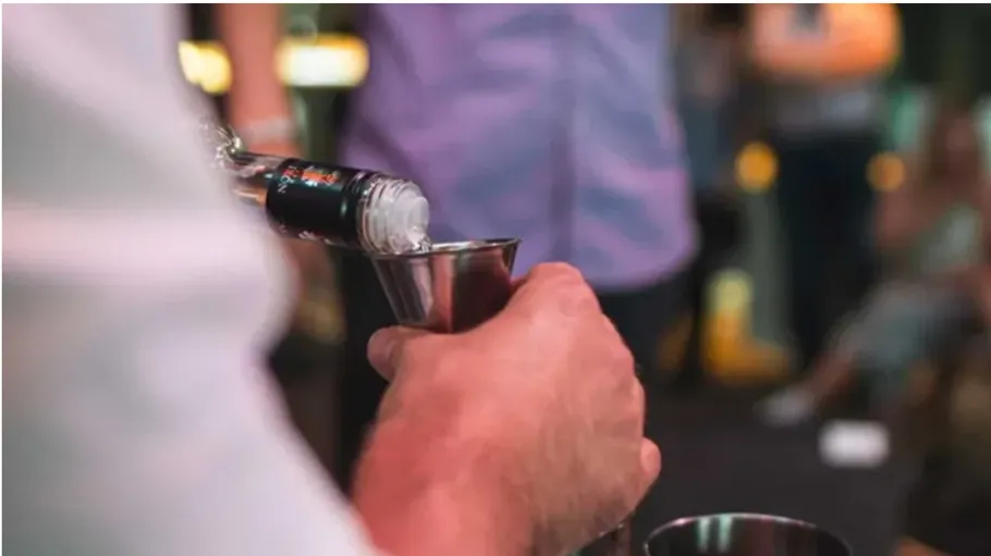 Person pouring liquid into jigger at bar.