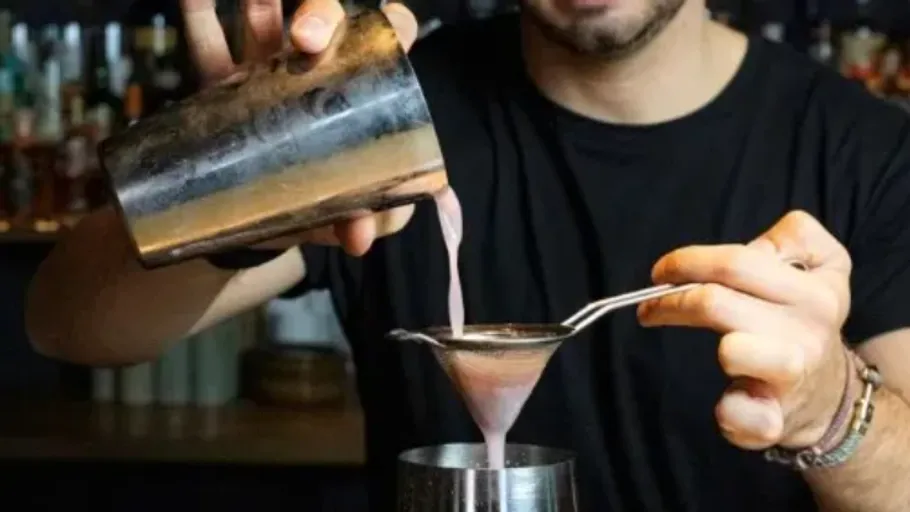 Barkeeper seiht Cocktail in Metallshaker ab.