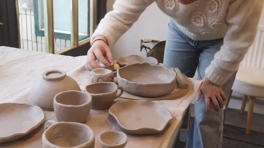 Person arranging unfinished clay pottery on table.