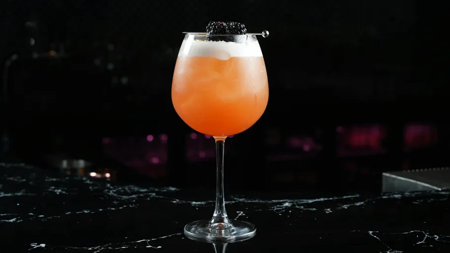 Orange cocktail with blackberry on dark counter.