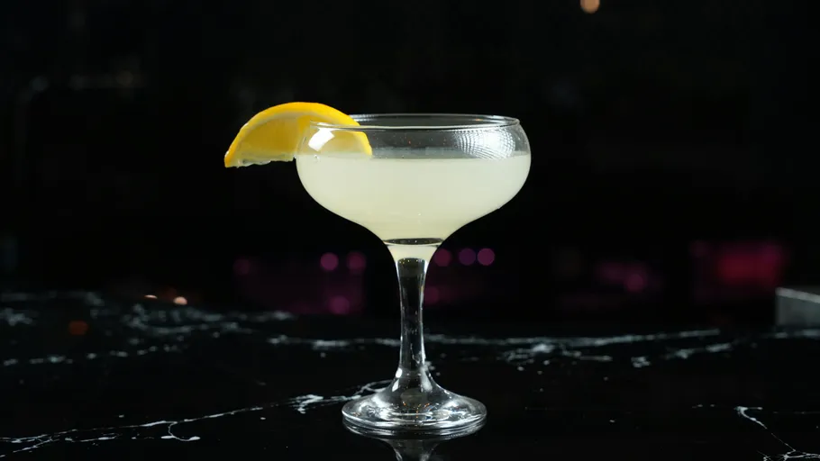 Cocktailglas mit Zitronengarnitur auf dunkler Bar.