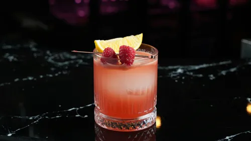 Cocktail with raspberries on dark bar.