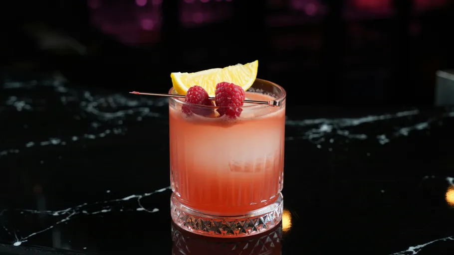 Cocktail with raspberries on dark bar.