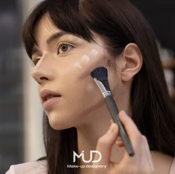 Frau trägt Make-up mit Pinsel drinnen auf.