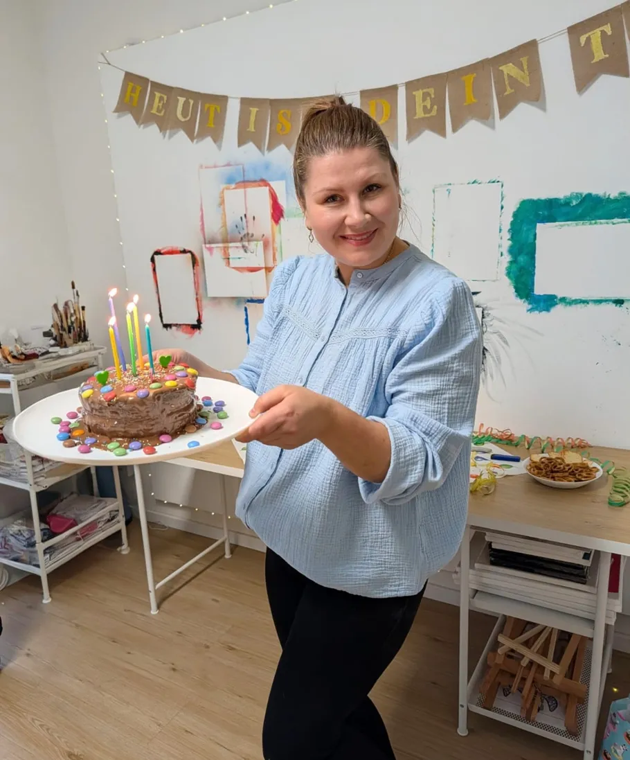 Woman holding decorated birthday cake indoors.