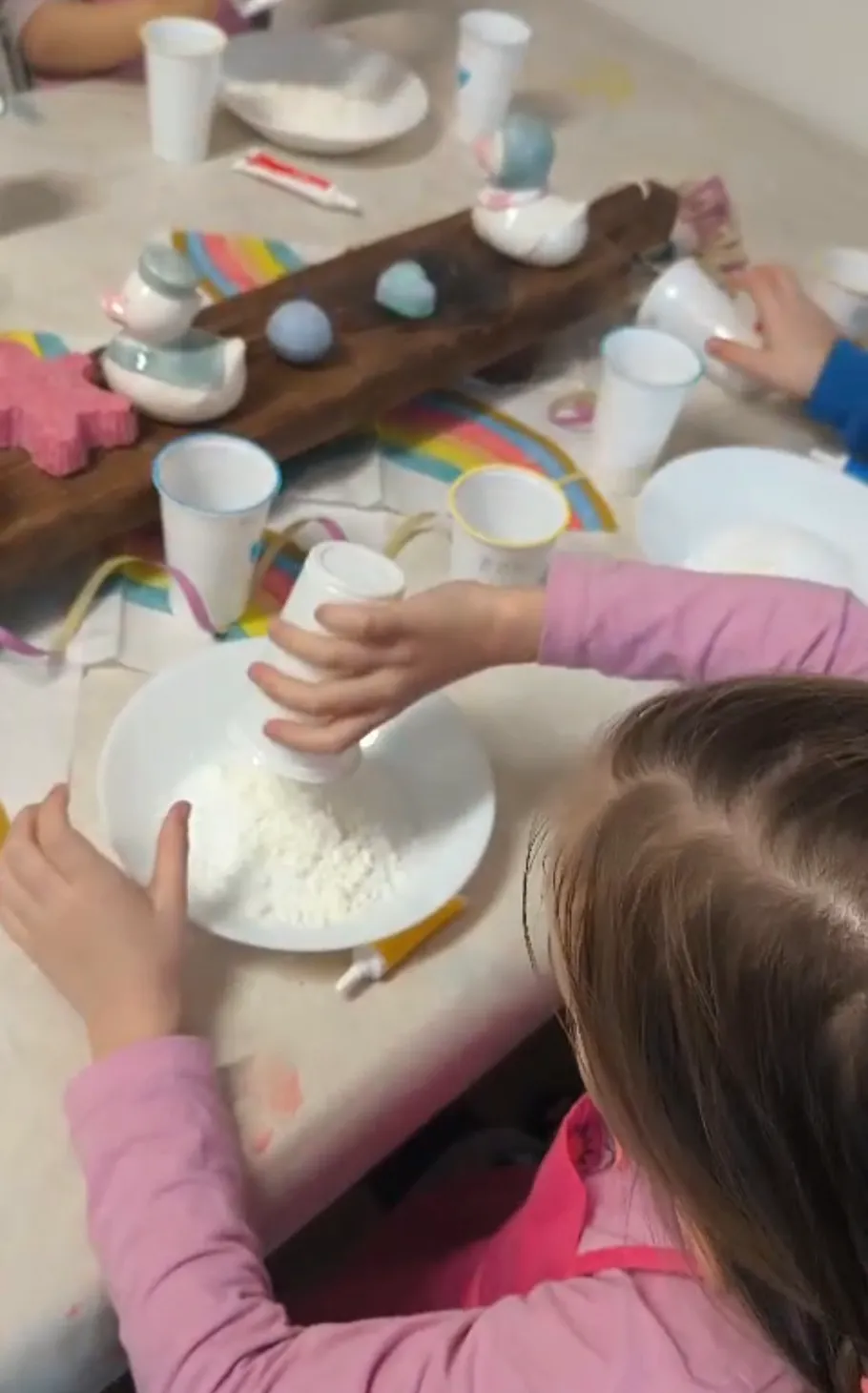 Child pouring powder into a bowl on table.