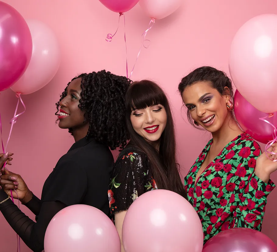 Three women smiling, holding pink balloons.