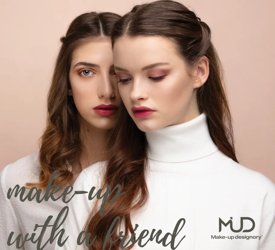 Two women posing against a beige background.