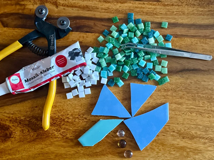 Mosaic tools, tiles and glue on wooden surface.