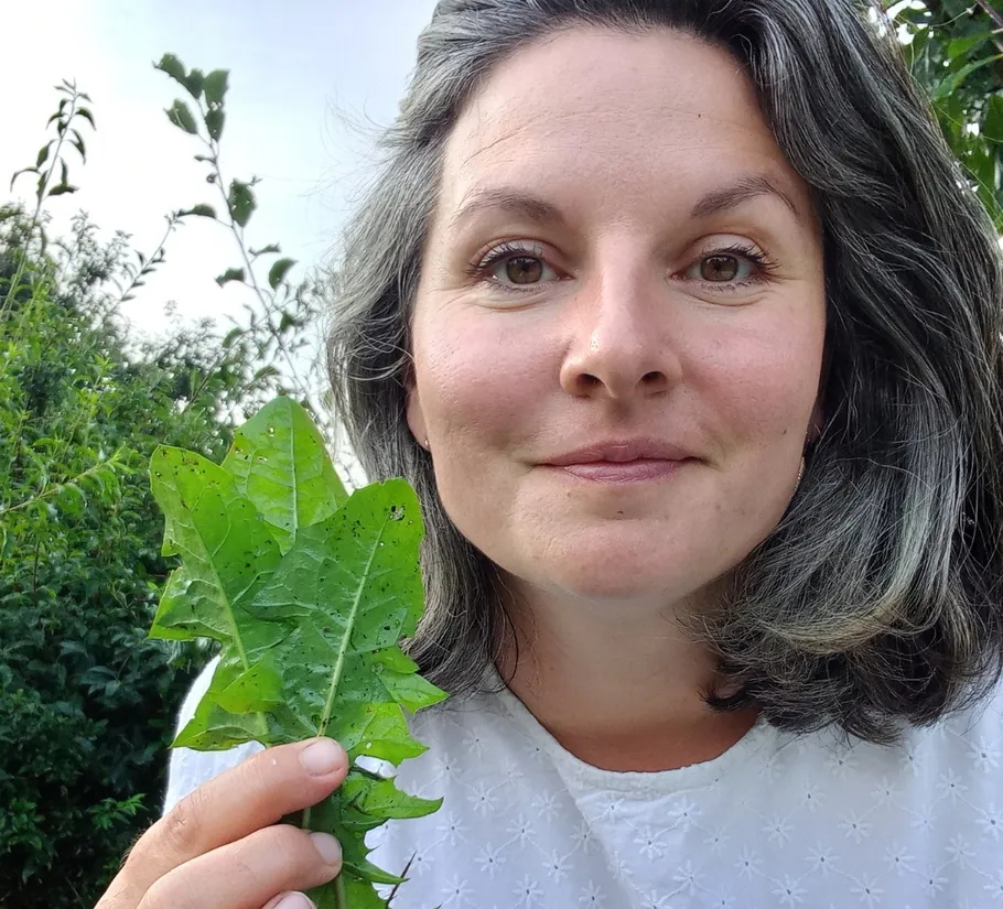 Person holding green leaves outdoors.