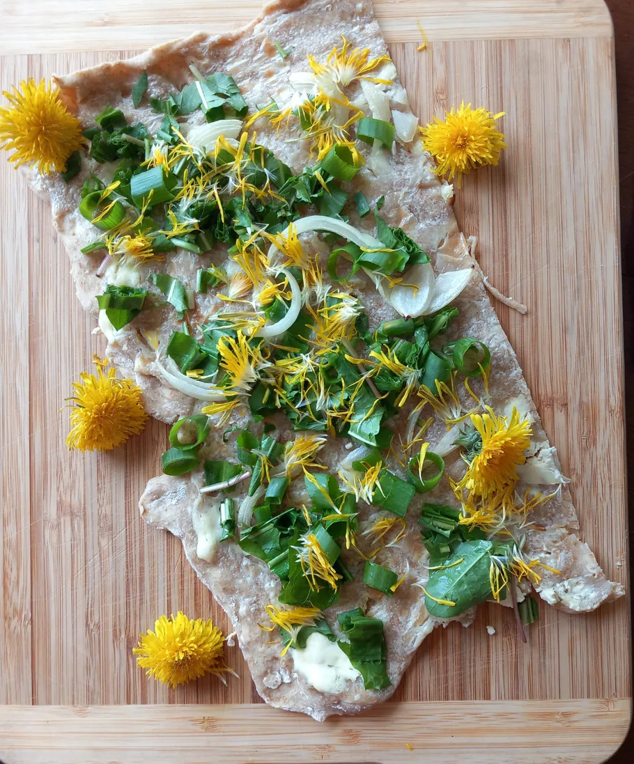 Fladenbrot mit Grünzeug und Löwenzahn auf Brett.