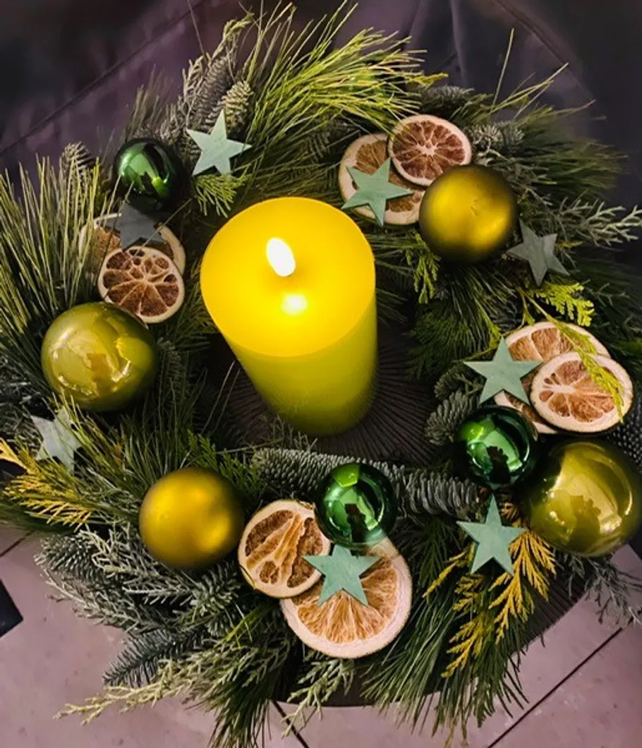 Yellow candle in festive wreath with greenery.