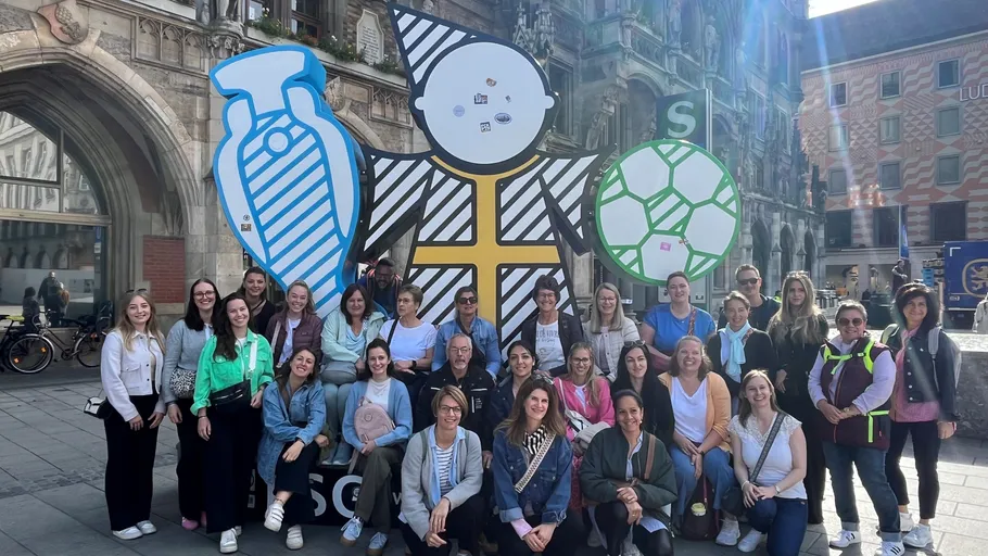 Group posing with colorful statue in city square.