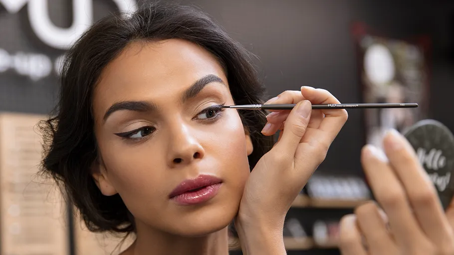 Woman applying eyeliner with brush in mirror.