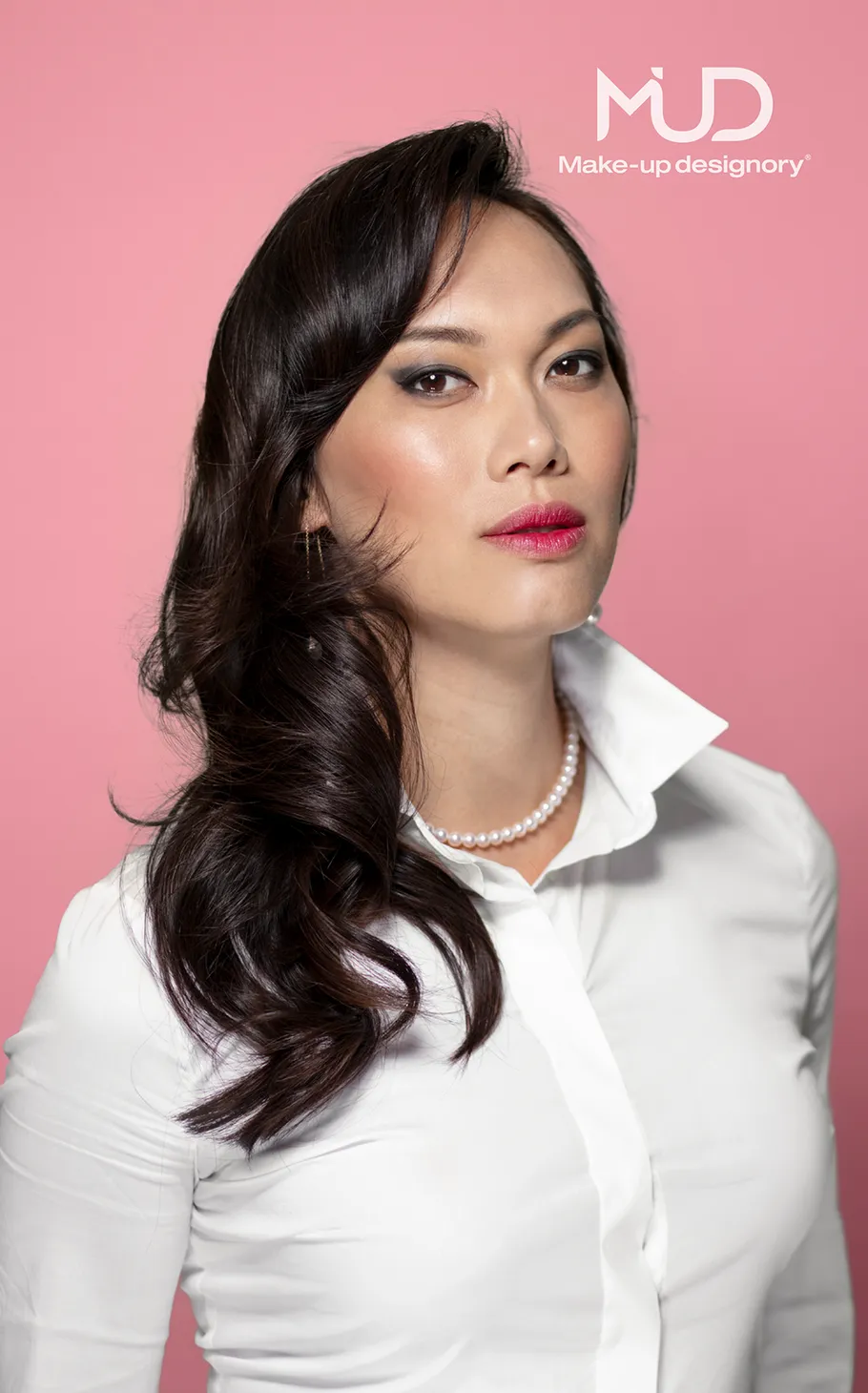Person posing against pink background, wearing white shirt.