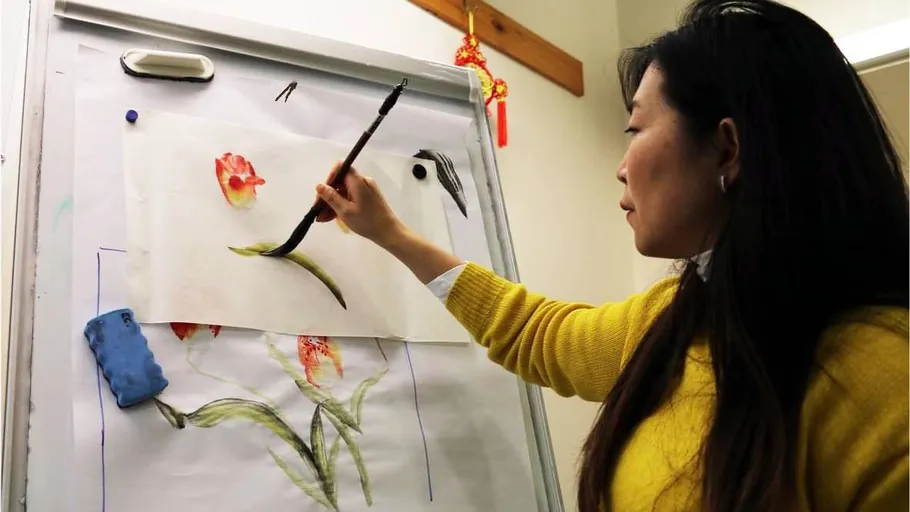 Frau malt Blumen auf Staffelei mit Pinsel.