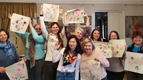 Group of people holding floral paintings indoors.