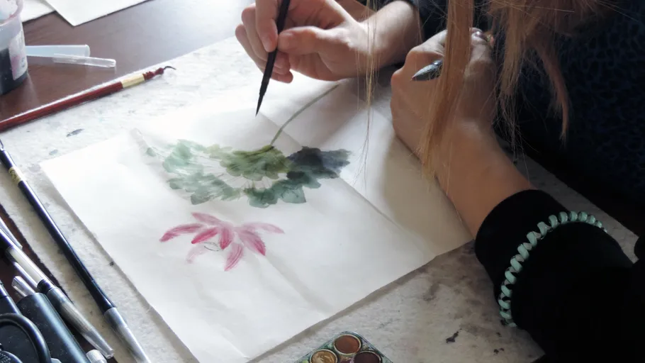 Person painting floral design on paper.