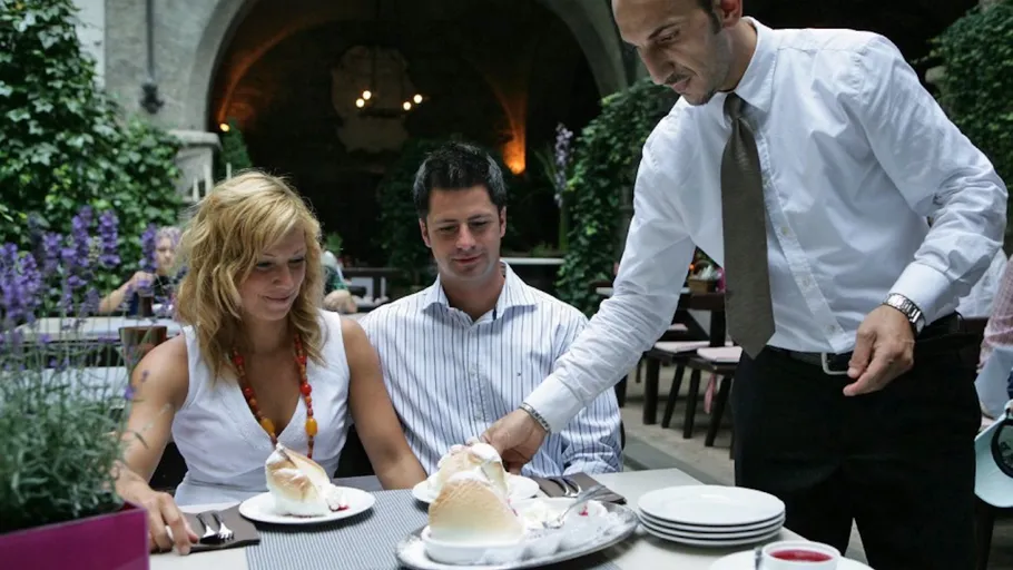Waiter serving desserts to a couple outdoors.