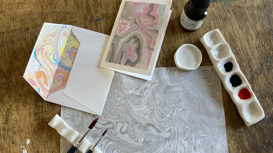 Marmorpapiere, Pinsel, Farben auf Holztisch.