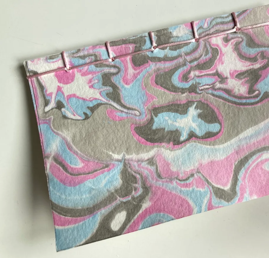 Notizbuch mit Marmorierung und rosa Bindung.