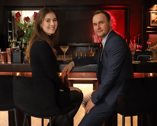 Two people sit at a bar smiling.