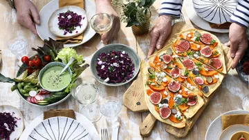 Menschen teilen buntes Essen auf Holztisch.