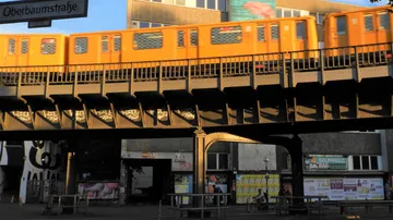 Oranger Zug überquert Hochbahn, städtische Umgebung.