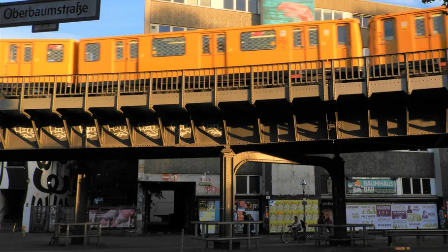 Orange train crossing elevated tracks, urban setting.