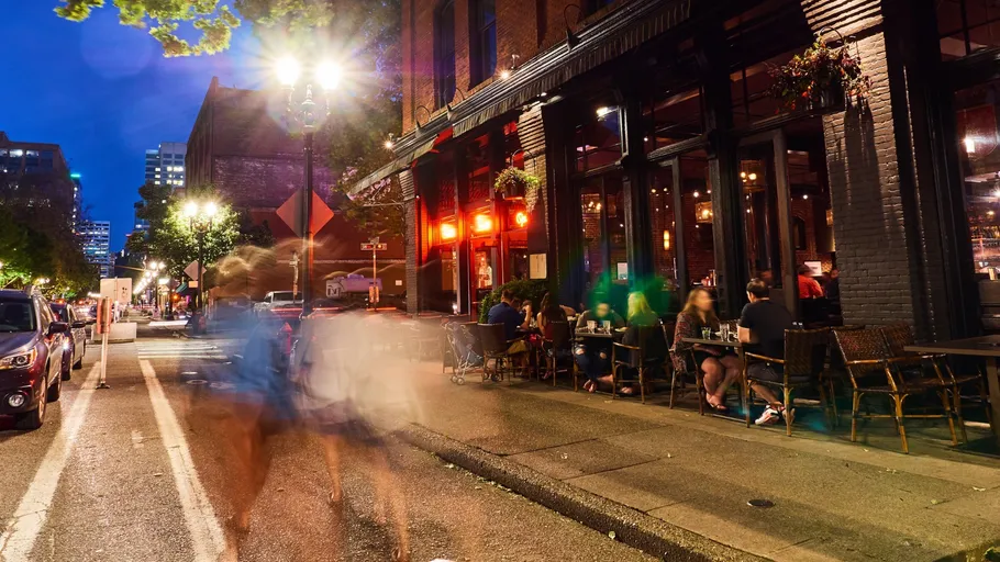 People walking past outdoor café at night.