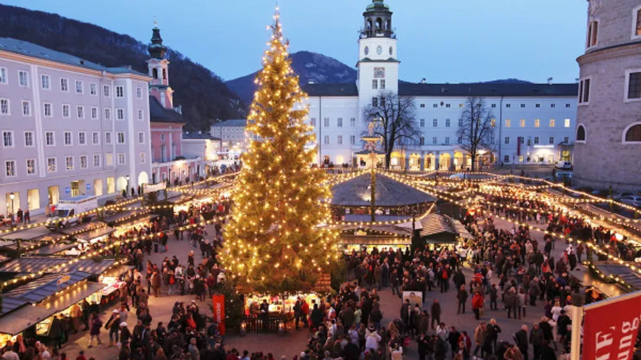Großer Weihnachtsmarkt mit beleuchtetem Baum bei Dämmerung.