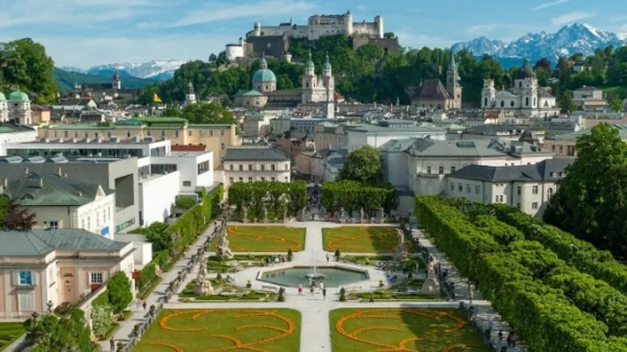 Cityscape with garden and castle, mountainous background.