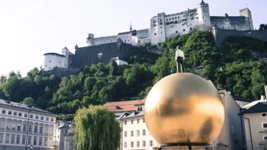 Golden statue on sphere, fortress in background.