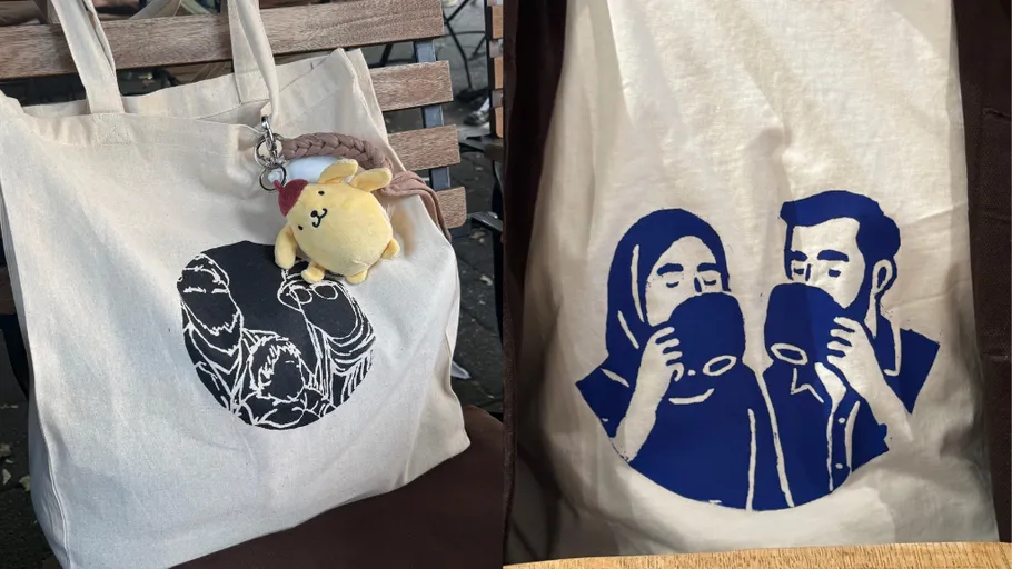 Stofftaschen mit Illustrationen auf einer Bank.