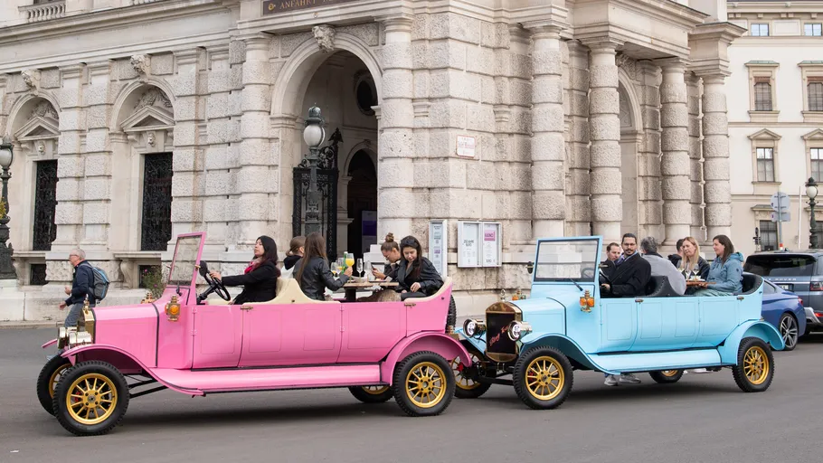 Two vintage cars, pink and blue, with passengers.
