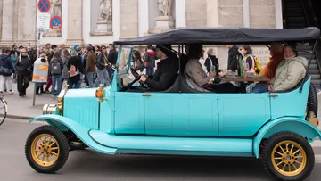 Vintage car driving with passengers, city street.