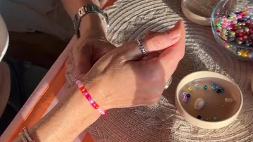 Hand wearing pink bracelet, crafting beads nearby.