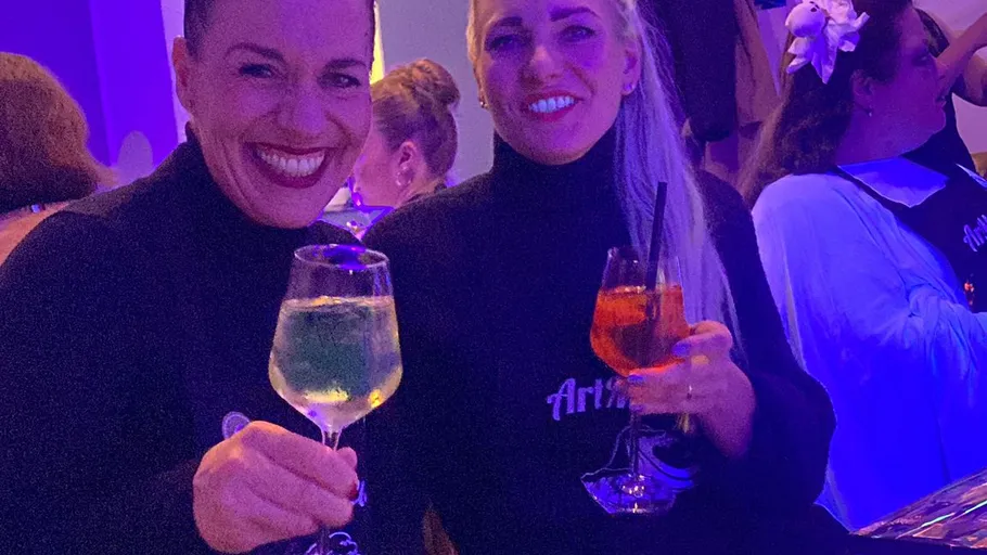Two women smiling with drinks, indoors.