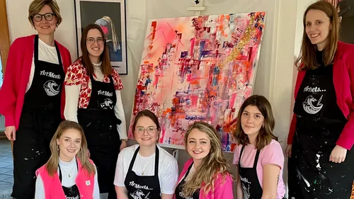 Group of women posing with abstract painting indoors.