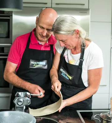 Two people are preparing dough in a modern kitchen.