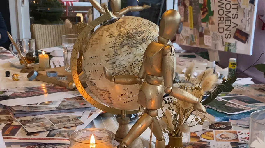 Wooden figure holding globe on cluttered table.