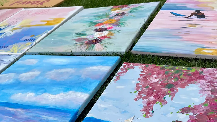 Paintings displayed outdoors on grass.