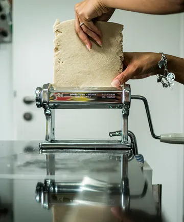 Teig wird durch eine Nudelmaschine auf einem Tisch gedrückt.