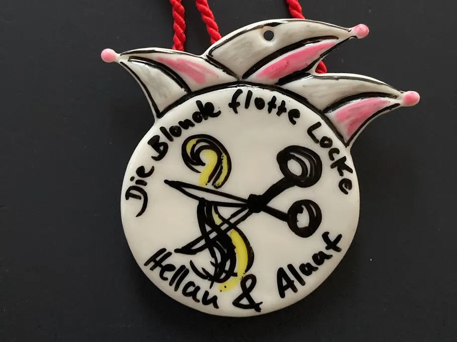 Ceramic medallion with text and scissors image.